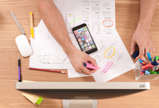 Top-down view of a person sketching marketing charts and plans on paper with a tablet and colorful p