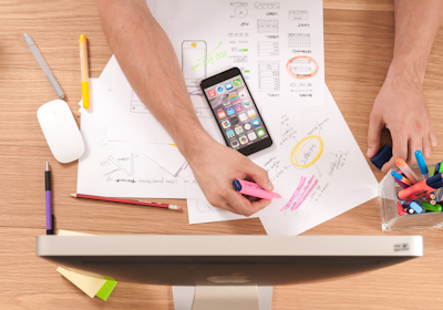 Top-down view of a person sketching marketing charts and plans on paper with a tablet and colorful p