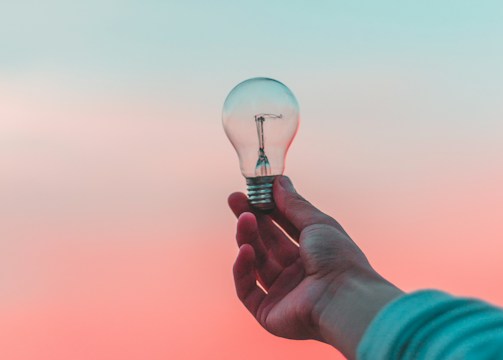 Hand holding glowing lightbulb against sky representing results-driven strategies