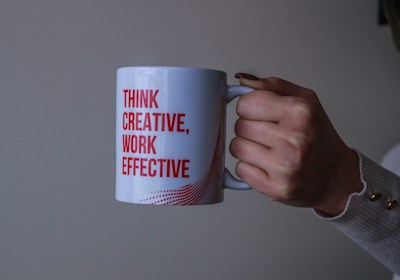 Hand holding a coffee mug that reads "Think Creative, Work Effective" symbolizing creative and effec