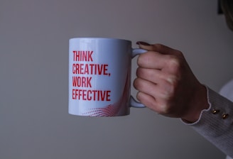 Hand holding a coffee mug that reads "Think Creative, Work Effective" symbolizing creative and effec